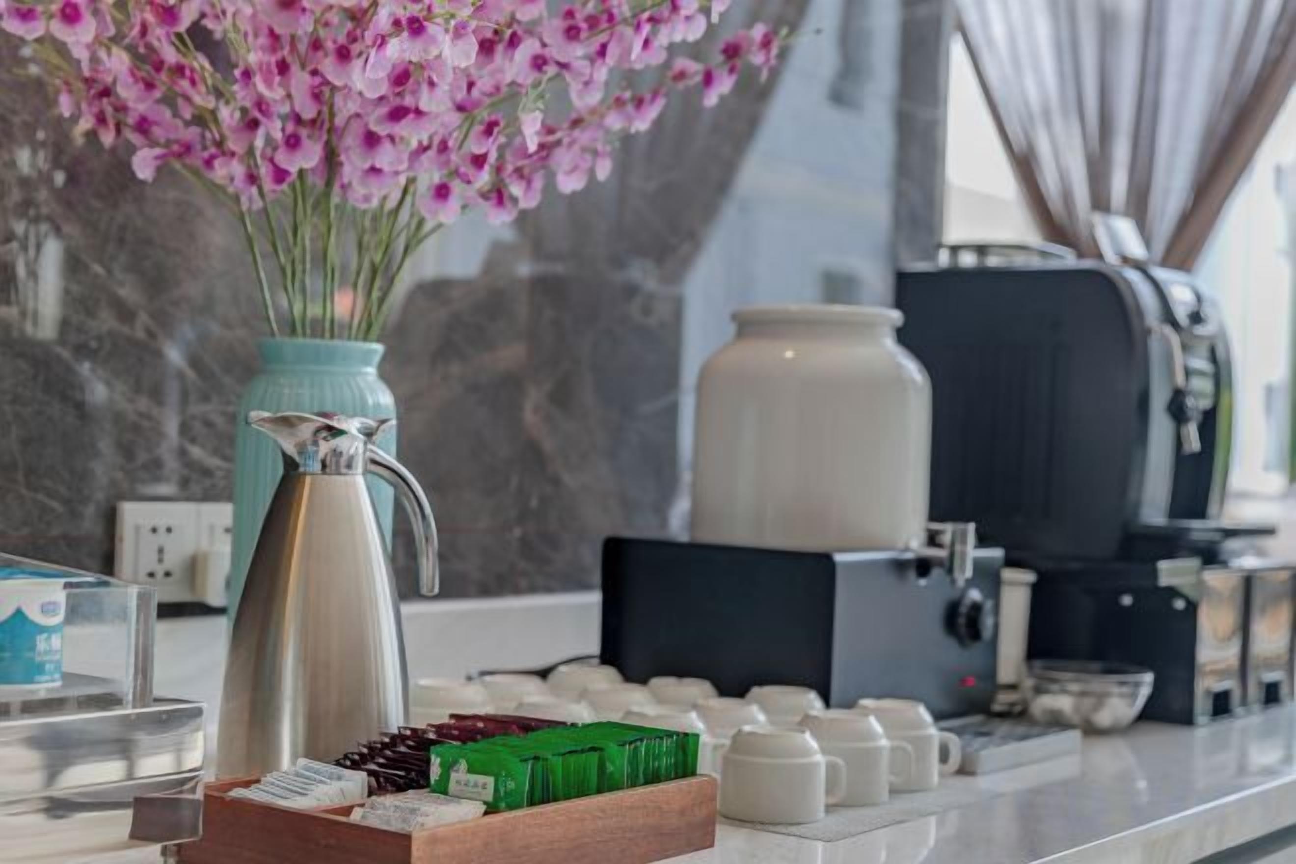 A coffee station with a coffee maker, a vase with flowers, and a tray of coffee cups.