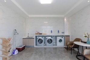 Een kleine keuken met een wasmachine, een spoelbak en een eethoek met stoelen.