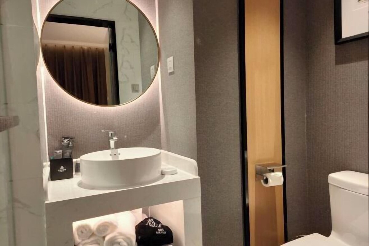 Une salle de bain moderne avec un miroir rond, un lavabo blanc et des toilettes.