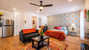 A compact living space with a kitchenette, a sofa, a bed, and a patterned wall.