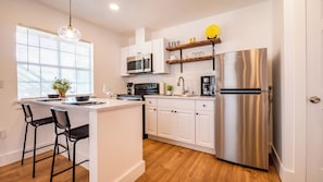 A modern kitchen with white cabinets, stainless steel appliances, a central island with bar stools, and a window with blinds. - Collins Garden First Floor Room, Pet Friendly (San Antonio)