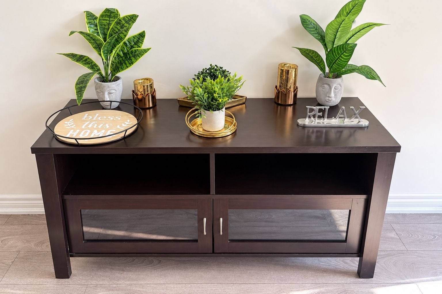 A dark wooden console table with three potted plants, a decorative tray, and a sign with the text 'bless this home.'