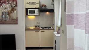 Een kleine keuken met een magnetron, fornuis en keukenkastjes, die uitkomt op een eethoekje.