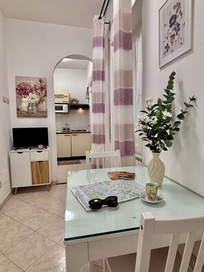 Un comedor con una mesa de vidrio, sillas, un florero con flores, un control remoto y un mapa.