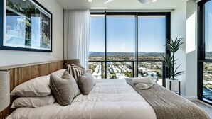 A bedroom with a large bed, a ceiling fan, and a view of a cityscape through large windows.