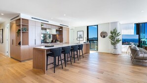 A modern kitchen with a central island, bar stools, and a large window offering a view of the outdoors.