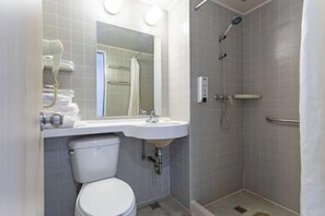 Et badeværelse med toilet, vask, spejl, brusebad og håndklædestang.