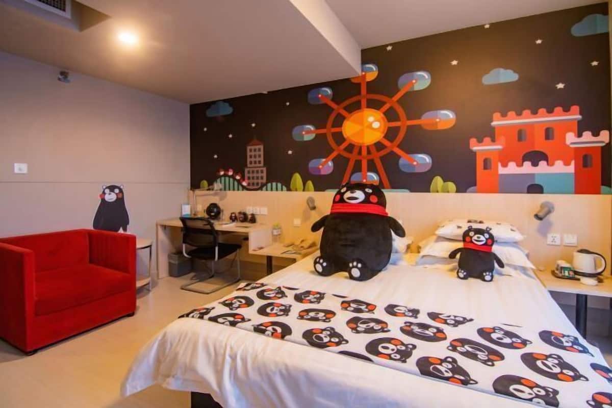 A hotel room with a bed, a red chair, a desk, and a wall mural.