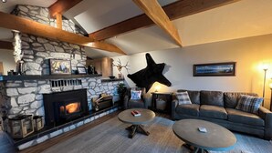 Una sala de estar acogedora con una chimenea de piedra, una gran escultura de cabeza de venado montada en la pared, un sofá gris y una mesa de centro.