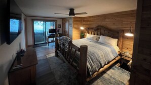 Un dormitorio con cabecera de madera, cama con ropa de cama a rayas, un escritorio con computadora y una puerta corrediza de vidrio que da a un balcón.