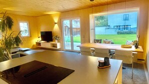 Una cocina moderna con una isla central, televisor integrado y un amplio ventanal corredera que da a un jardín.