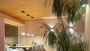 Una sala de estar moderna con un sofá, una zona de comedor con sillas y una planta grande en maceta.