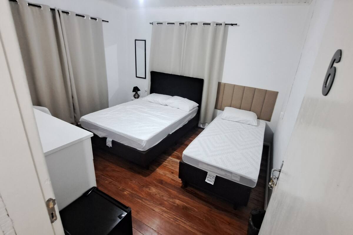 A small, compact room with two single beds, a small desk, and a trash bin.