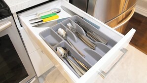 Un tiroir de cuisine contenant des ustensiles et un outil dont le manche est vert.