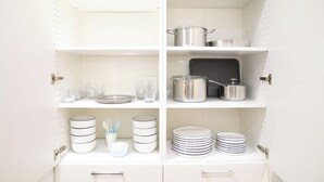 Un meuble de cuisine blanc, doté de plusieurs étagères, où sont rangés divers ustensiles de cuisine, comme des assiettes, des bols et des casseroles.