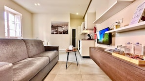 A modern living room with a sofa, a small table, a TV, and a kitchen area in the background. - Stylish 1 Bedr Apt next to The sea Front (Il-Gzira)