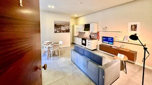 A modern living room with a sofa, a dining table with chairs, a kitchen area, and a television. - Stylish 1 Bedr Apt next to The sea Front (Il-Gzira)
