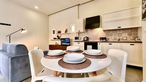 Un espacio habitable compacto con zona de comedor, una mesa redonda con sillas blancas y un sofá gris.