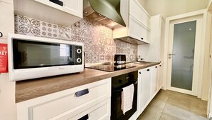 Una cocina moderna con armarios blancos, microondas, cafetera y horno empotrado.