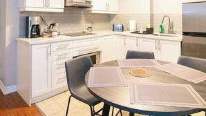 A modern kitchen with white cabinets, a built-in oven, a stainless steel refrigerator, and a dining area with a round table and chairs.