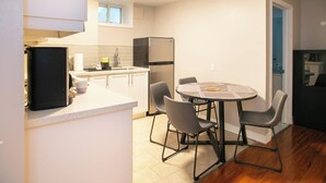 A compact kitchen with a dining area, featuring a refrigerator, sink, and a small table with chairs.