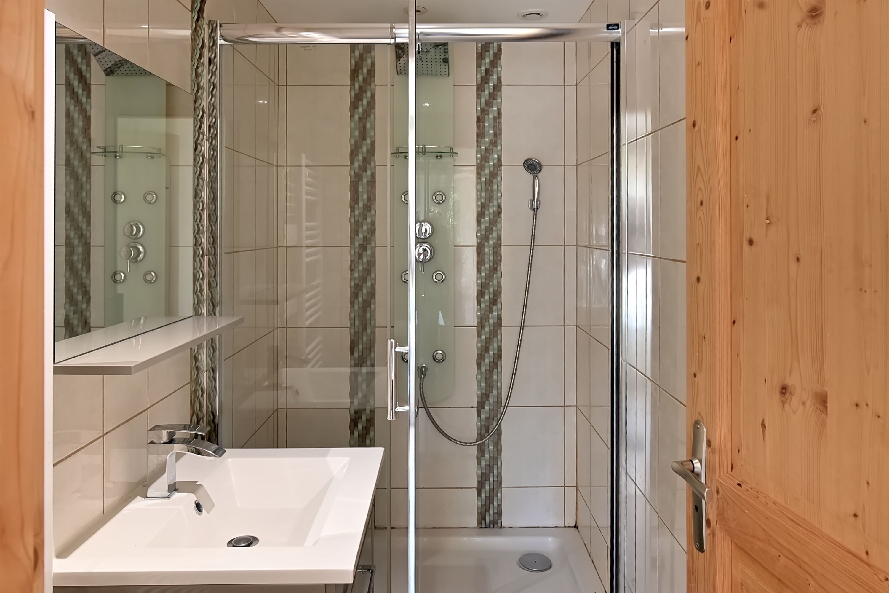 Un bagno moderno con doccia vetrata, un lavandino bianco e una porta in legno.
