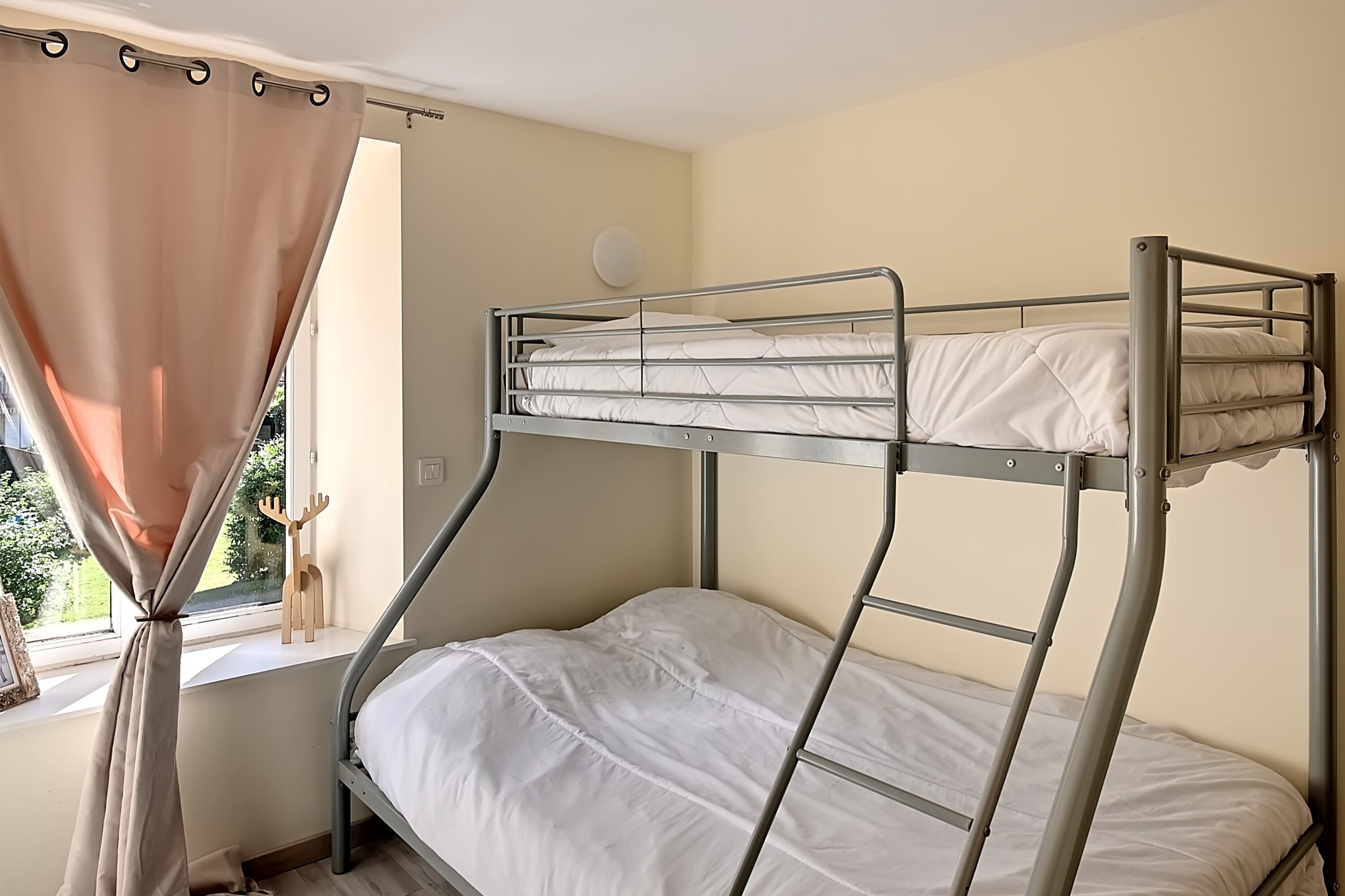 A bunk bed in a room with a window, curtains, and a wall-mounted light.