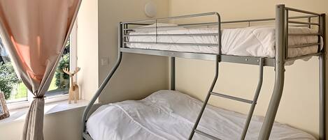 A bunk bed in a room with a window, curtains, and a wall-mounted light.