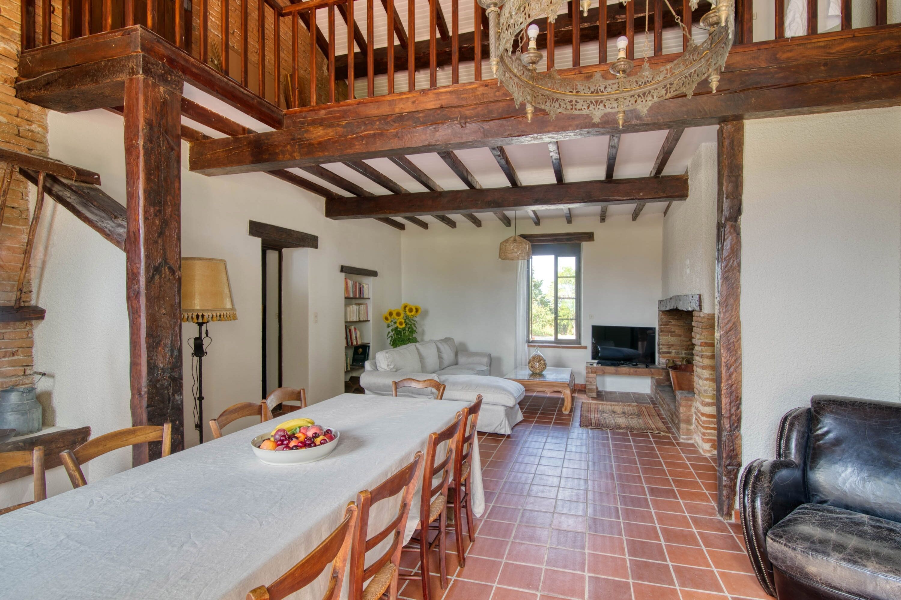 A rustic interior with exposed wooden beams, a dining area with a table and chairs, a sofa set, and a leather couch.
