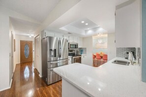 A modern kitchen with stainless steel appliances, a large island, and a dining area with orange chairs. - Spacious Beach Bungalow | 4BR w/ Pool & Game Room (Largo)