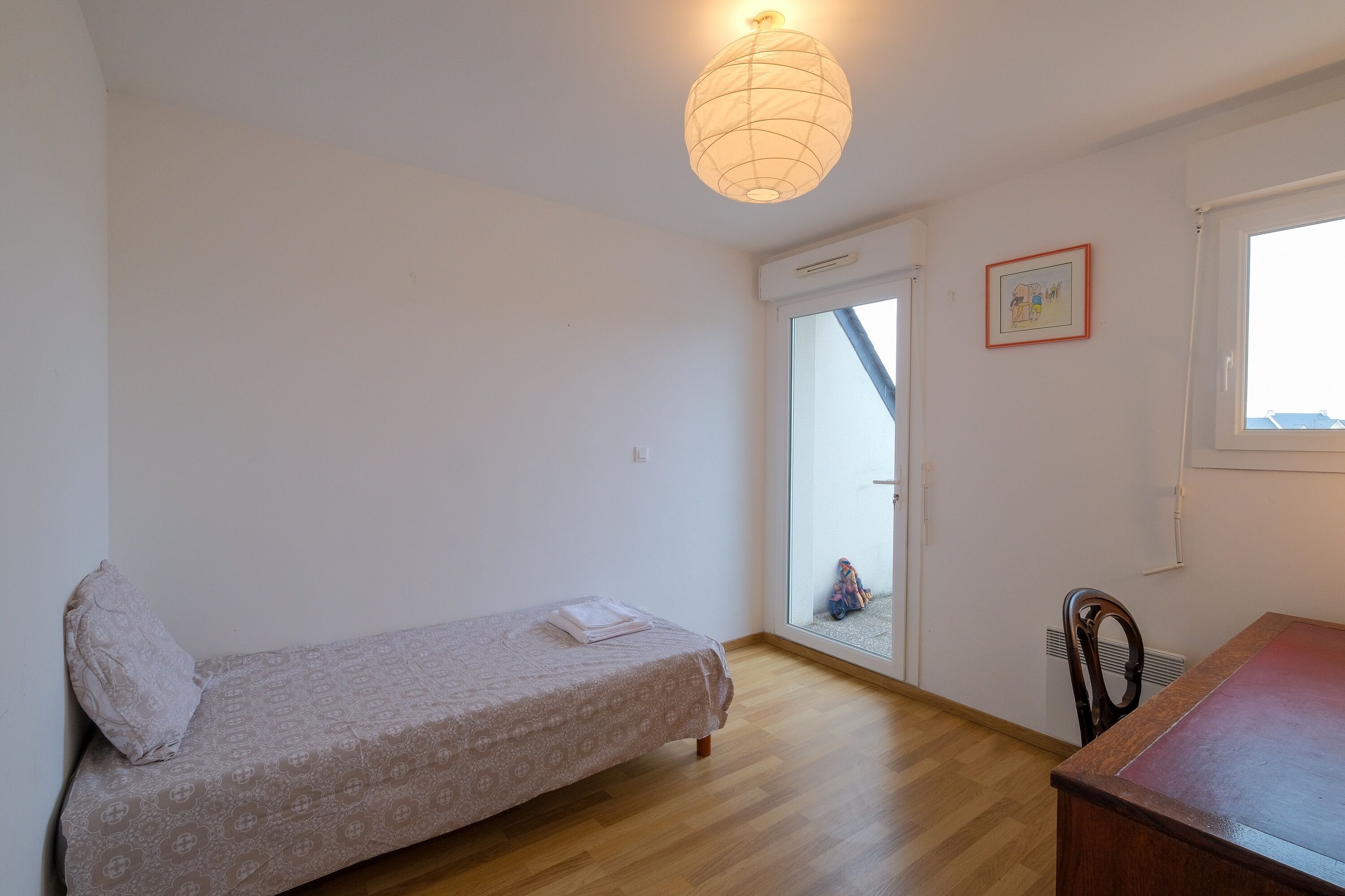 A small, clean room with a single bed, a chair, a table, and a window.