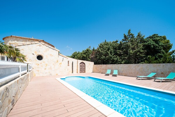 A swimming pool with a stone wall and a wooden deck. - Casa Jade - Appt pour 4 (Fitou)