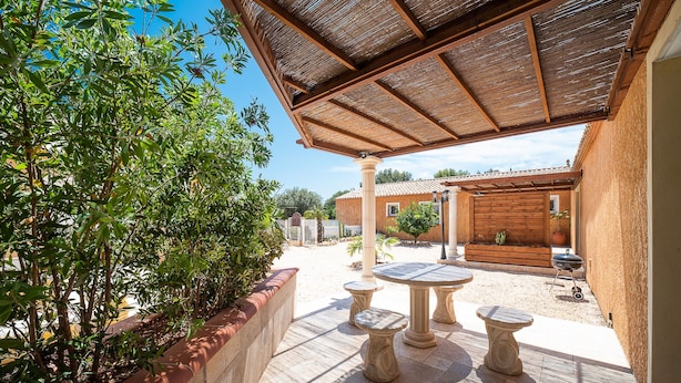 An outdoor patio with a wooden pergola, stone tables, and a brick wall with greenery.