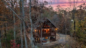 A cabin with a deck and multiple levels, surrounded by trees.