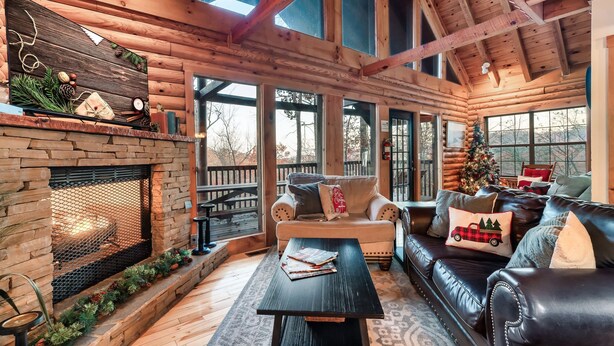 A cozy log cabin interior with a stone fireplace, leather sofa, and a Christmas tree.