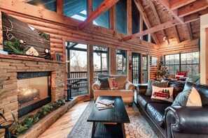 A cozy log cabin interior with a stone fireplace, leather sofa, and a Christmas tree.