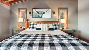A bedroom with a checkered bedspread, a wooden headboard, two bedside tables with lamps, and a framed picture of a bull on the wall.