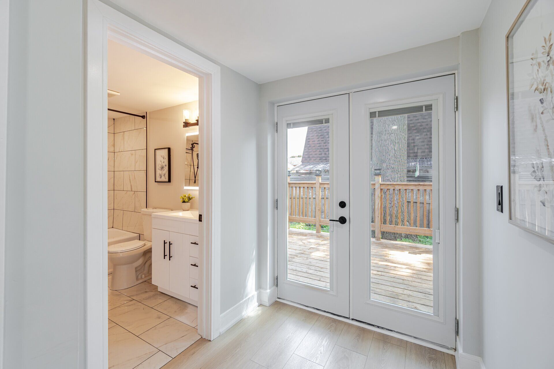A bathroom with a toilet, sink, and mirror, and a door leading to a wooden deck.