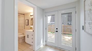 A bathroom with a toilet, sink, and mirror, and a door leading to a wooden deck.