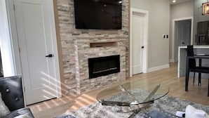 Un salon moderne avec une cheminée en pierre, un téléviseur à écran plat fixé au mur et une table basse en verre.