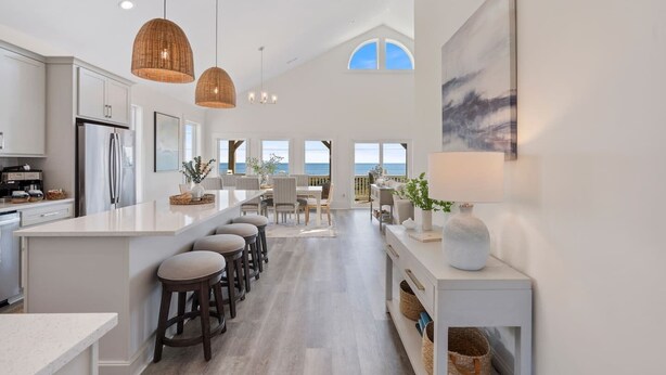 A spacious kitchen with a central island, bar stools, and a view of the ocean through large windows.