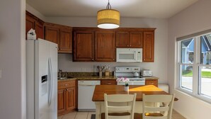 Una cocina con armarios de madera, un refrigerador blanco, un microondas, un lavavajillas y una mesa de comedor con dos sillas.