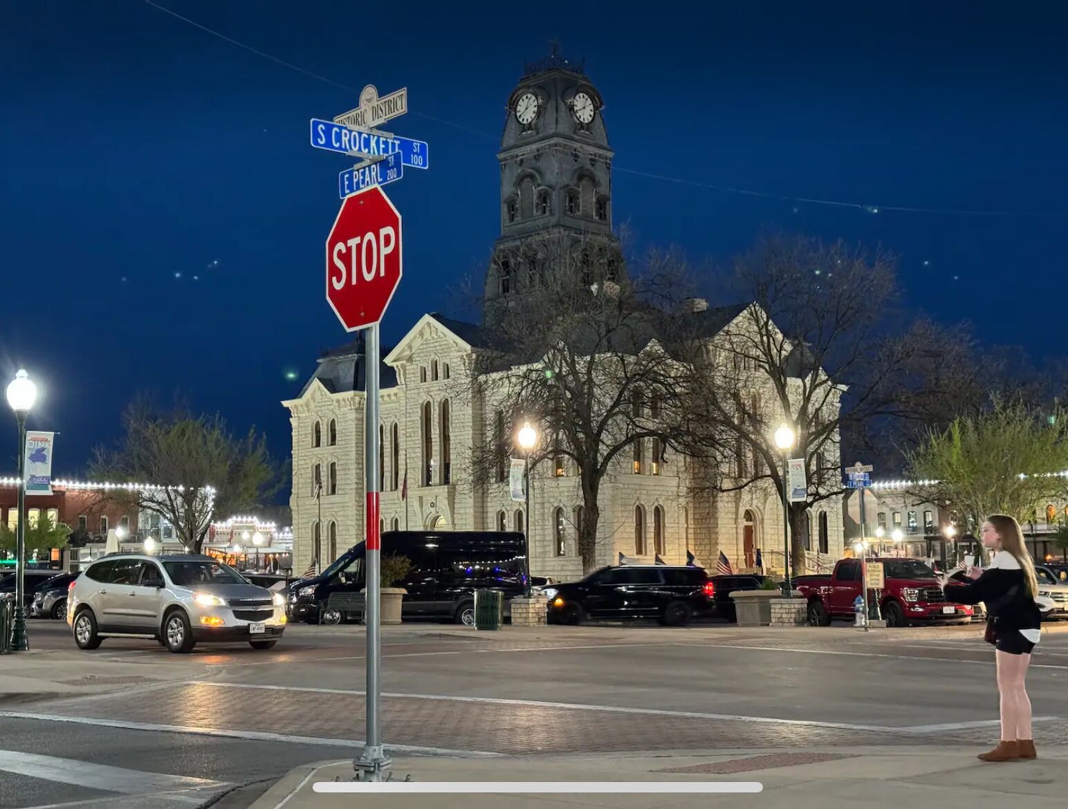 A historic building with a clock tower, a stop sign, and street signs at a nighttime intersection.
