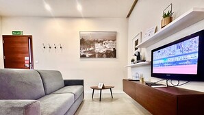 A modern living room with a grey sofa, a coffee table, a flat-screen TV, a wall-mounted picture, and a fire exit sign.