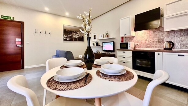 A modern kitchen with white cabinets, a flat-screen TV, and a dining area with a white table set for four.
