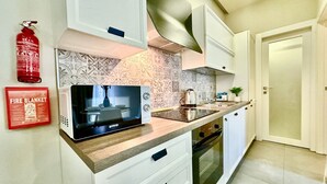 A modern kitchen with white cabinets, a microwave, a stove, and a fire extinguisher.