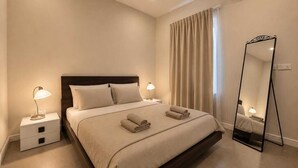 A hotel room with a bed, bedside lamps, a mirror, and an air conditioning unit.