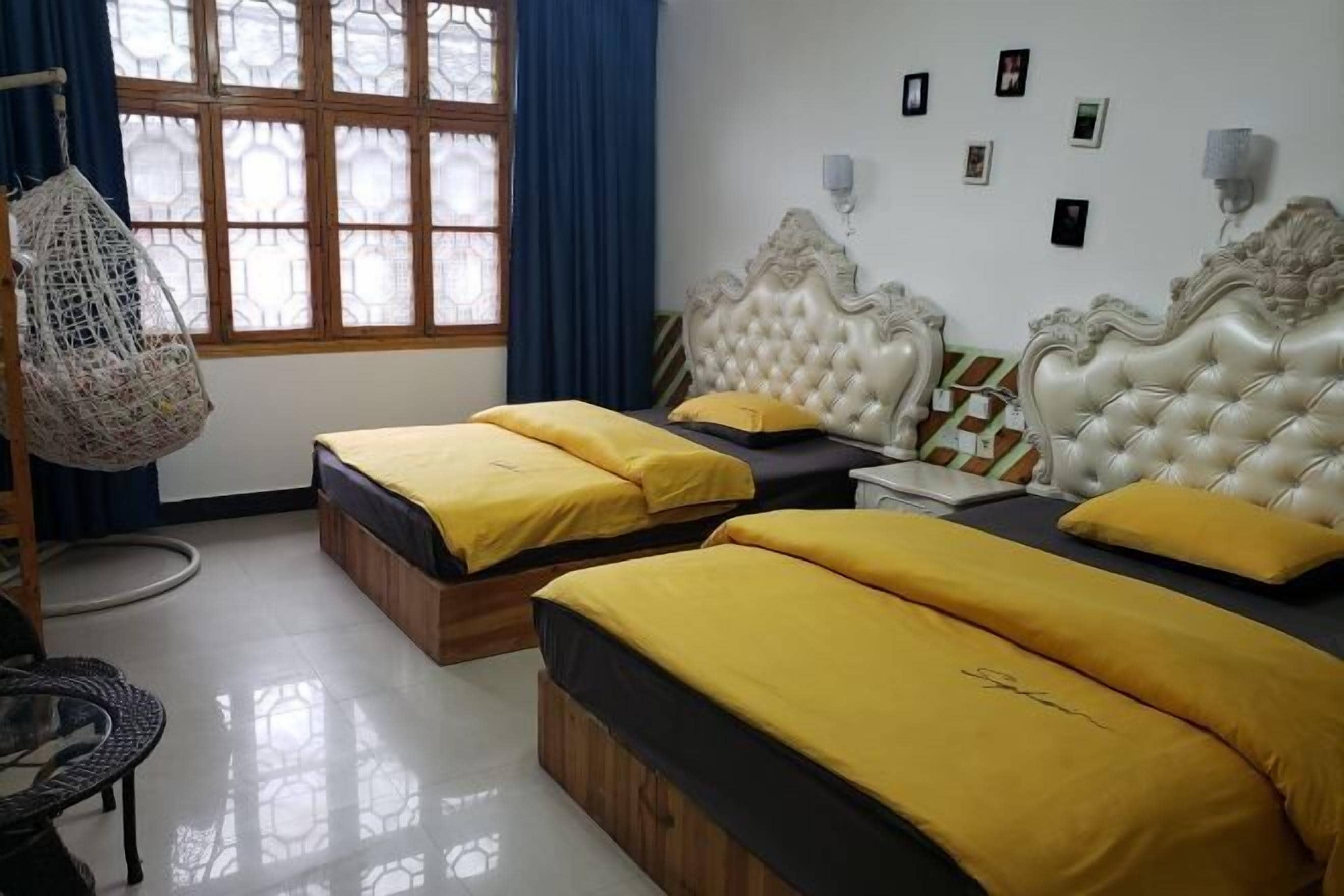 A room with two beds, a hanging chair, and a window with blue curtains.