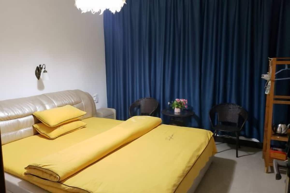 A room with a bed, two chairs, a small table with flowers, and a shelf with items.