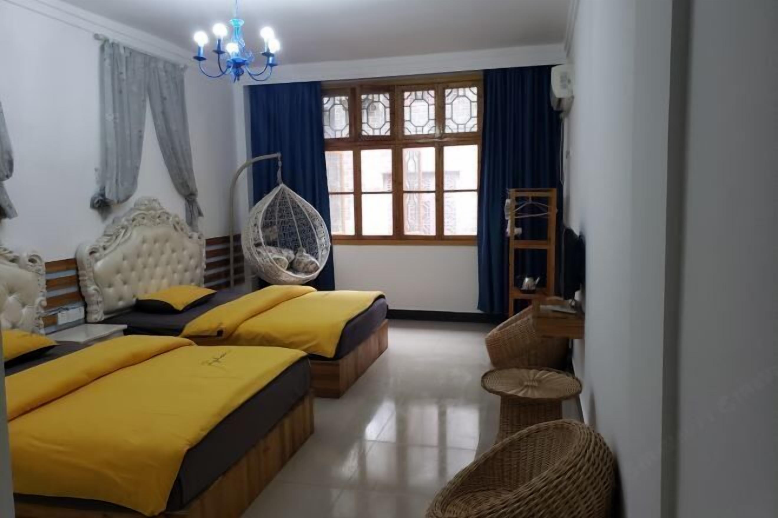 A hotel room with three beds, a hanging chair, a wooden ladder, and a large window with curtains.